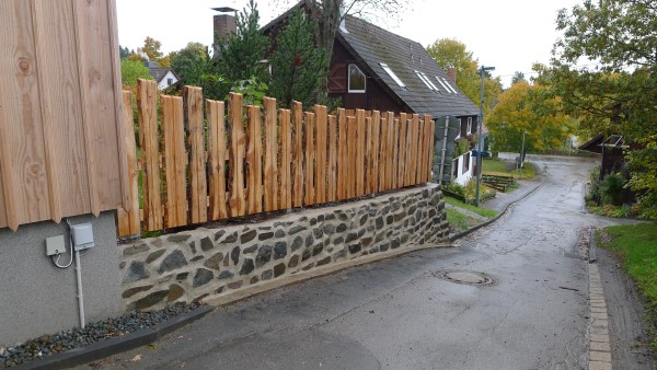 Aus Natursteinen erstelltes Böschungsmauerwerk mit Zaun aus Lärchenholz